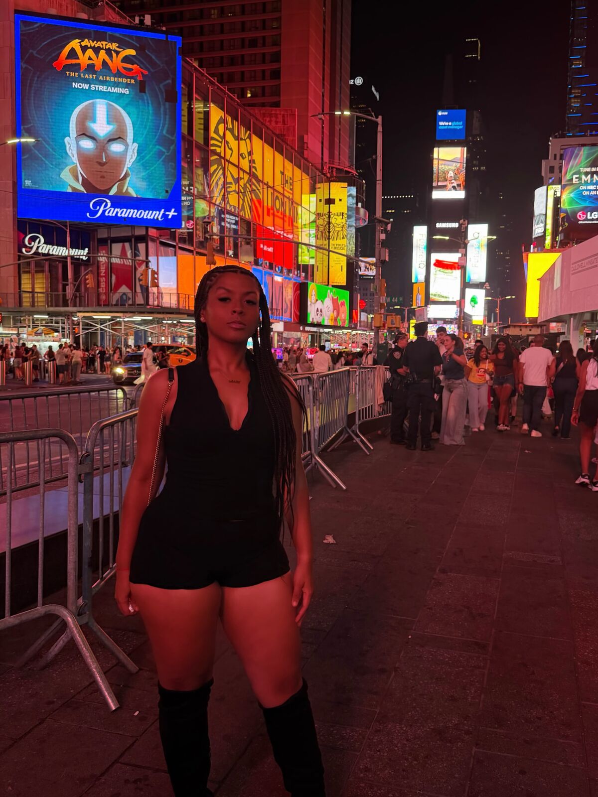 LA Real Ash in Times Square at night, black outfit and knee-high boots, glowing billboards behind her