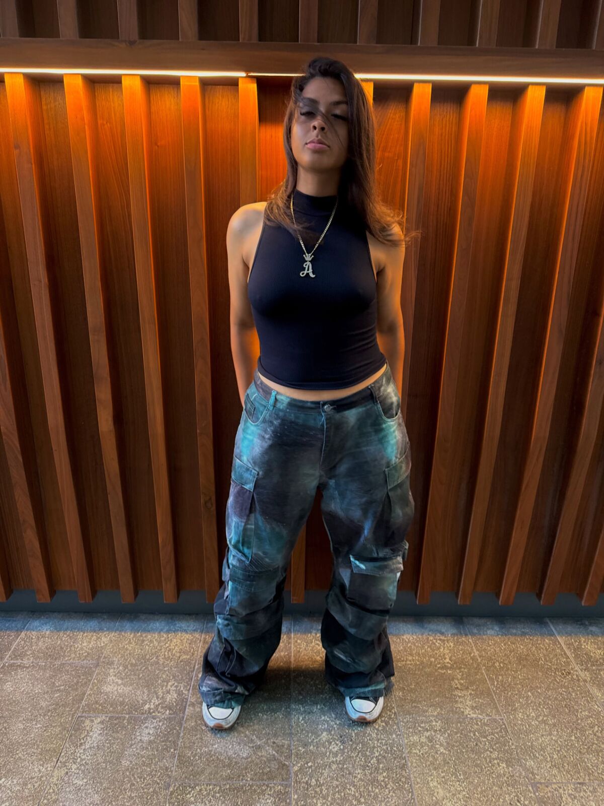 Full-body shot of LA Real Ash in a black sleeveless top and baggy blue patterned jeans with sneakers